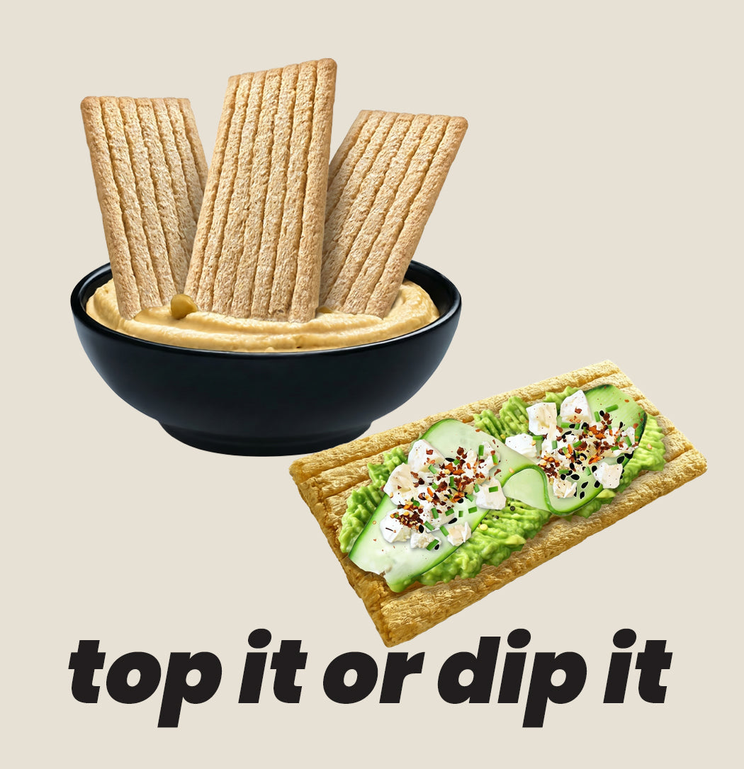 Bowl of hummus with maszfita crispbread slices and a crispbread with avocado spread on a beige background.